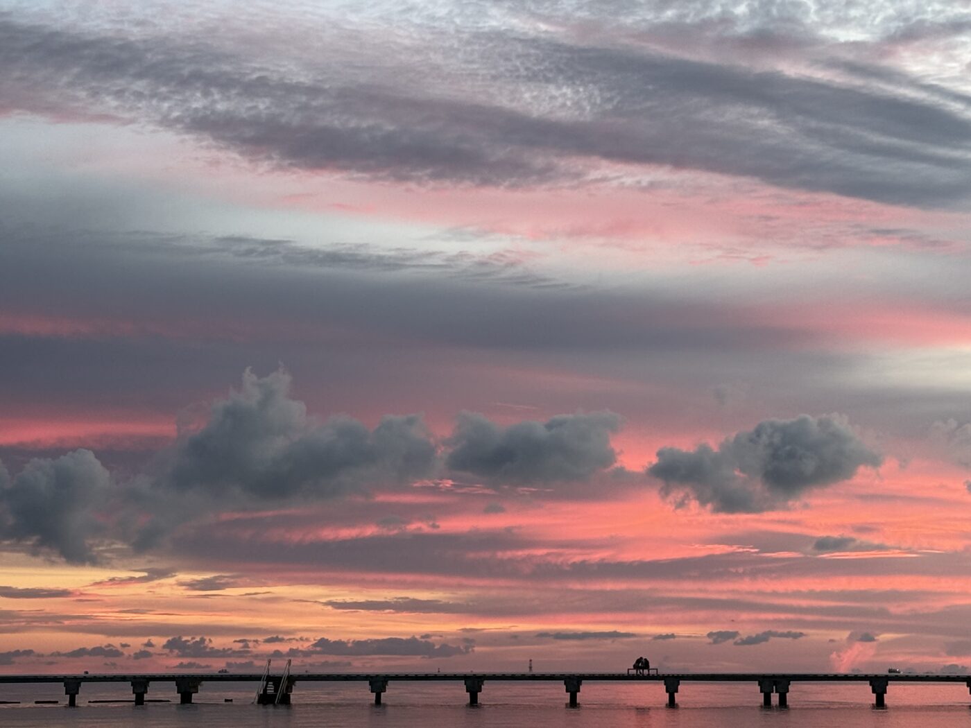 Two people sitting together at the end of a pier as the sky turns pink over the water in the Florida Keys